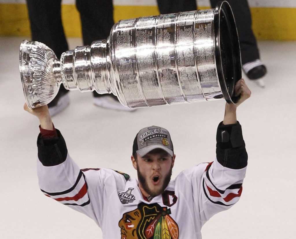 On-ice photo of Jonathon Toews hoisting the Stanley Cup above his head in 2013