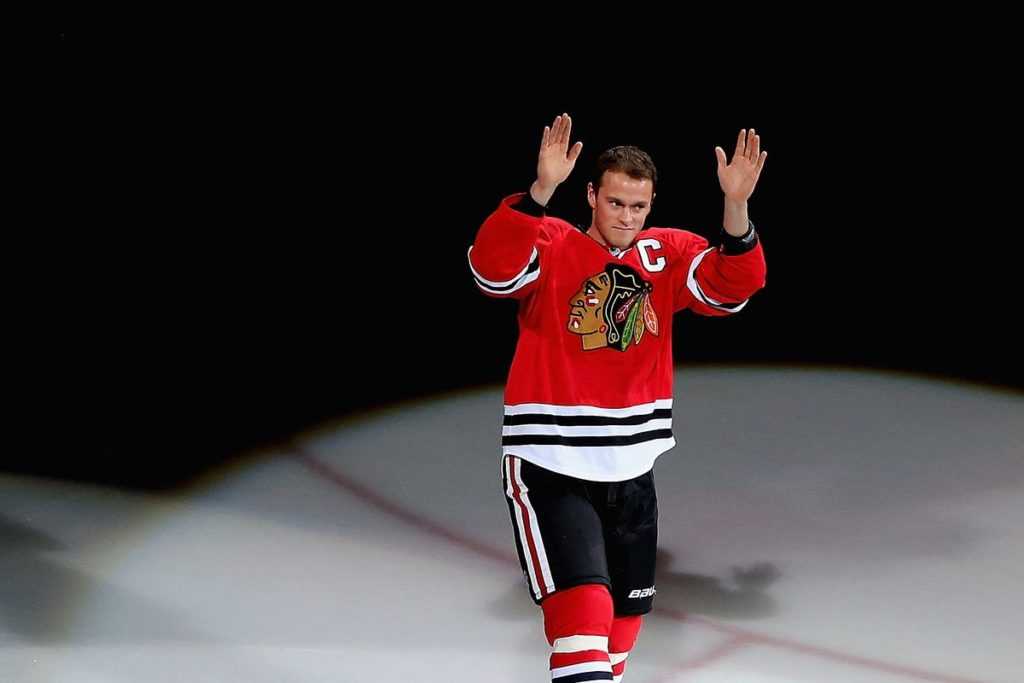 On-ice photo of Jonathan Toews in spotlight, waving thank you to fans at The United Center.