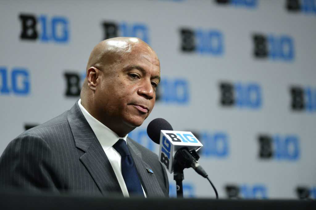 Big Ten Commissioner Kevin Warren talks to reporters amidst his myriad of questionable decisions.  He is sitting behind a microphone speaking to media
