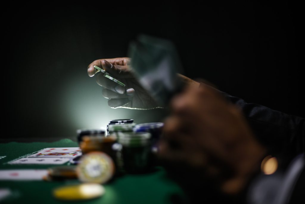 A hand holding a poker chip about to place it on a card table