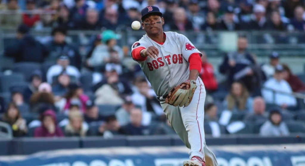 Rafael Devers has been a revelation on defense in 2022. Pictured: Rafael Devers in Red Sox road grey jerseys throwing the ball to first base. 