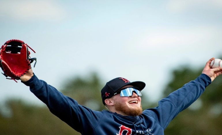 Pictured: Red Sox Alex Verdugo In blue sweatshirt with his hands raised in the air and smiling