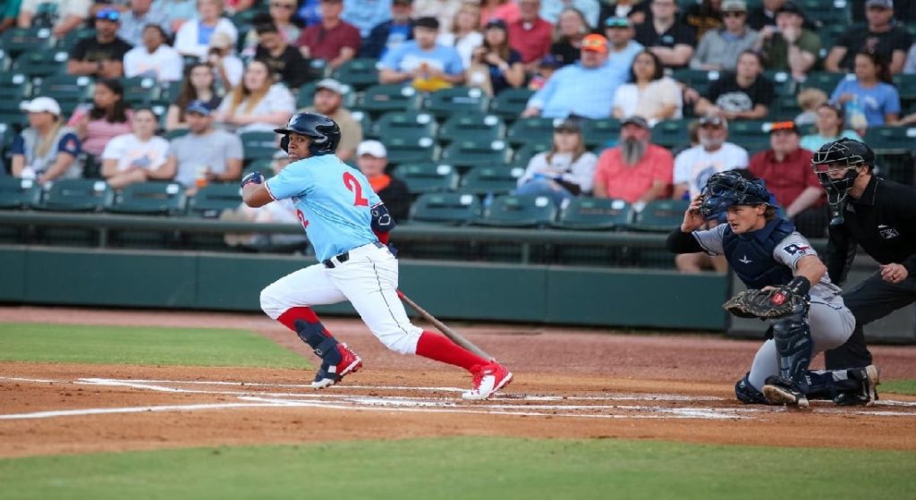 Pictured: Enmanual Valdez, acquired in the Christian Vasquez trade, is at-bat, wearing a light blue jersey top with a red number 2, and white jersey pants rolled up to his knees, exposing red socks. He is wearing a black helmet.